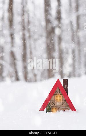 Miniaturhaus mit rotem Dach, tief im Schnee inmitten eines Waldes Stockfoto