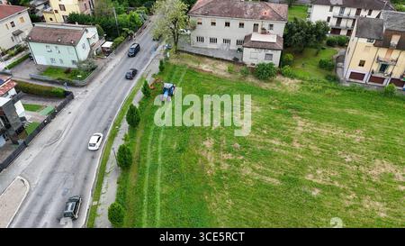 Castell'Arquato, Italien - 24. April 2025 Luftaufnahme eines blauen Traktors, der akribisch bewachsenes Gras und Unkraut auf einem ländlichen Feld in der Nähe eines Dorfes schneidet Stockfoto