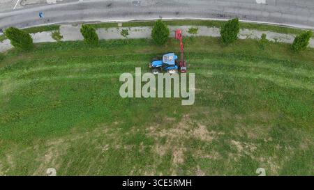 Landwirtschaftliche Maschinen, die fleißig arbeiten, um bewachsene Vegetation und widerspenstiges Unkraut von einem weiten Feld unter hellem Himmel zu befreien, das ländliche Land zeigt Stockfoto