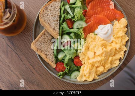 Blick von oben auf Rührei, Räucherlachs, gemischten Salat, Mehrkornbrot und Frischkäse auf einem Tisch mit Eishummel Stockfoto