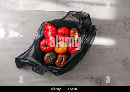 Ein Netzbeutel gefüllt mit verschiedenen Erbtomaten auf einer strukturierten Oberfläche. Stockfoto