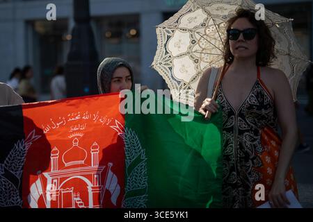 Madrid, Spanien. August 2025. Frauen halten eine afghanische Flagge und einen Regenschirm während einer Demonstration in der Puerta del Sol in Madrid für die Rechte der afghanischen Frauen. Am 15. August jährt sich der vierte Jahrestag der Eroberung Kabuls durch die Taliban, ein Ereignis, das ihre Rückkehr an die Macht in Afghanistan nach dem Abzug der US- und NATO-Truppen markiert. Seither hat sich die Lage des Landes drastisch verschlechtert, insbesondere was die Menschenrechte angeht. Quelle: SOPA Images Limited/Alamy Live News Stockfoto