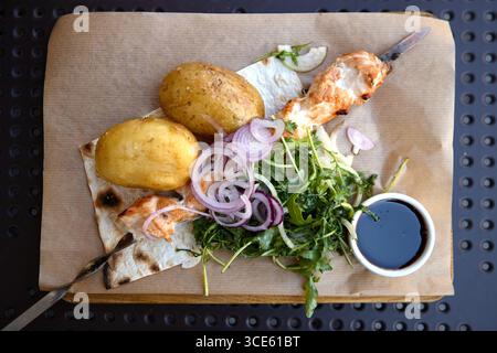 Gericht mit gegrillten Hähnchenspießen, gekochten Kartoffeln, grüner Beilage und Sauce Stockfoto