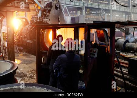 Die Arbeiter betreiben in der Gießerei Kreiselgießmaschinen für Eisenrohre. Stockfoto