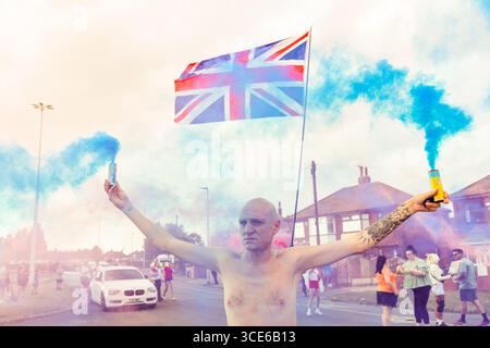 Leeds, Großbritannien. AUGUST 2025. Ein Demonstrant hält bunte Fackeln, wie in der vierten Woche, in der sich gegnerische Gruppen von Pro- und Anti-Migrant-Demonstranten am Straßenrand in der Nähe des Britannia Hotels in Seacroft, Leeds, versammelten. Die Demonstranten der 'Stand Up Leeds' zündeten mehrere Fackeln an, und drei Gegenprotestierende wurden verhaftet, nachdem es zwischen Aktivisten und Polizei zu Streitigkeiten gekommen war. Credit Milo Chandler/Alamy Live News Stockfoto