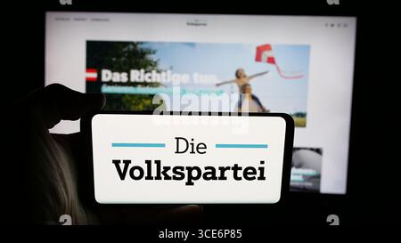 In dieser Foto-Illustration hält eine Person ein Handy mit dem Logo der ÖVP auf dem Bildschirm vor der Webseite. Stockfoto