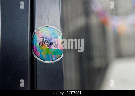 Farbenfroher, kreisförmiger Aufkleber mit „Jesus“-Text im Regenbogendesign mit leuchtenden Blau-, Rosa-, Grün- und Gelbtönen, die an einem dunklen Metallstab befestigt sind Stockfoto