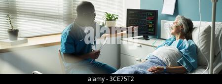 Schwarzer männlicher Arzt erklärt der älteren Kaukasierin die Ergebnisse des Herzmonitors Stockfoto