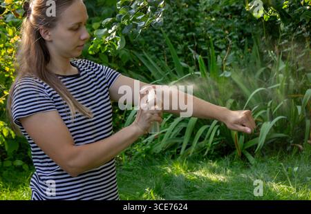 Frau, die im Sommer im Garten im Freien Mückenschutzmittel auf den Arm sprüht. Stockfoto