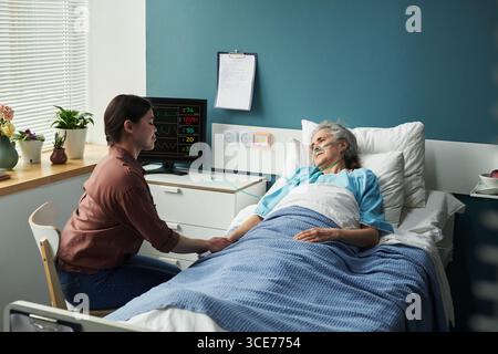 Junge kaukasische Frau tröstet ältere Frau, die im Krankenhausbett liegt Stockfoto