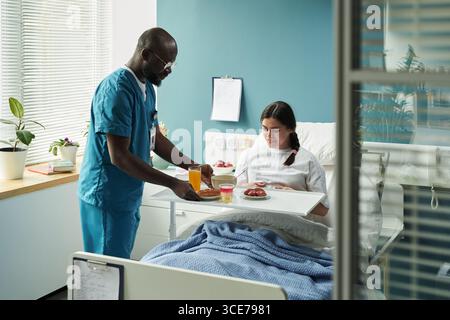Männliche Krankenschwester serviert Frühstück für junge schwangere Frau in der Entbindungsstation Stockfoto