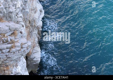 Wellen krachen sanft gegen zerklüftete weiße Klippen und erzeugen Schaummuster entlang des türkisfarbenen Meeres. Der dramatische Kontrast zwischen Felsen und Wasser. Stockfoto