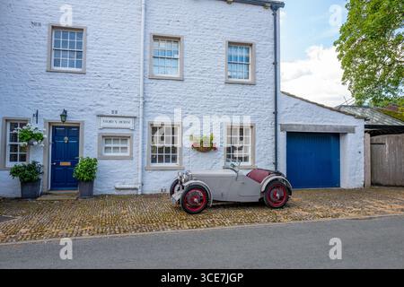 Vollständig restaurierte MG J2 Midget in Hellgrau gestrichen und auf einem Kopfsteinpflaster vor einem weiß gemalten Steinhaus stehend. Stockfoto