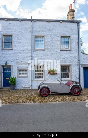 Vollständig restaurierte MG J2 Midget in Hellgrau gestrichen und auf einem Kopfsteinpflaster vor einem weiß gemalten Steinhaus stehend. Stockfoto