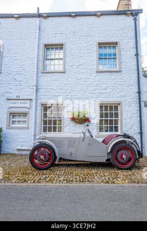 Vollständig restaurierte MG J2 Midget in Hellgrau gestrichen und auf einem Kopfsteinpflaster vor einem weiß gemalten Steinhaus stehend. Stockfoto