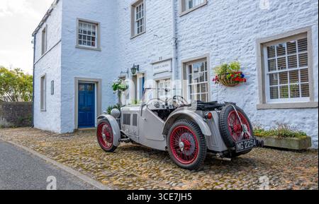 Vollständig restaurierte MG J2 Midget in Hellgrau gestrichen und auf einem Kopfsteinpflaster vor einem weiß gemalten Steinhaus stehend. Stockfoto