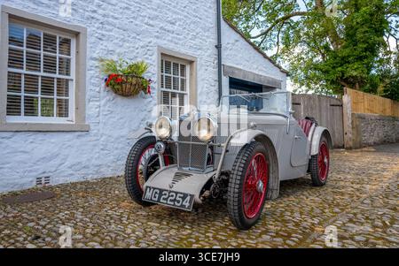 Vollständig restaurierte MG J2 Midget in Hellgrau gestrichen und auf einem Kopfsteinpflaster vor einem weiß gemalten Steinhaus stehend. Stockfoto