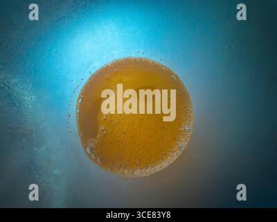 Nahaufnahme einer aufschäumenden Kaffeetasse von oben auf einer blauen Oberfläche mit Kondensation, wodurch ein abstraktes Muster entsteht, das sich perfekt für Kaffee-Backgro eignet Stockfoto
