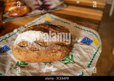 Frisch gebackenes Brot mit goldener Kruste auf besticktem Stoff. Rustikales hausgemachtes Brotkonzept mit natürlicher Textur und traditionellem Stil Stockfoto