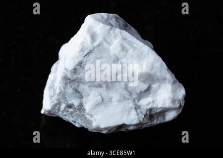Probe von rohem Howlithgestein auf schwarzem Granithintergrund aus nächster Nähe Stockfoto