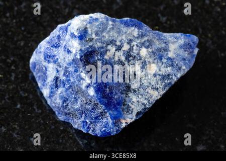 Probe von rohem Sodalitmineral auf schwarzem Granithintergrund aus nächster Nähe Stockfoto