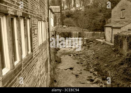 Ein sepiafarbener Blick auf den Luddenden Bach, der zwischen traditionellen Steinbauten fließt, mit einem kleinen Wasserfall im Hintergrund. Stockfoto