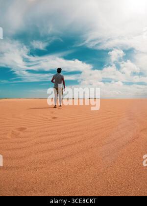 Ein einsamer Mann steht auf den pulsierenden Sanddünen von La Guajira, Kolumbien, unter einem hellblauen Himmel mit flauschigen weißen Wolken. Stockfoto