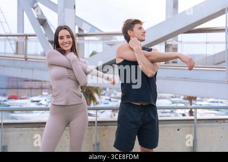 Lächelndes Paar, das die Arme vor dem Training auf der Außenterrasse streckt Stockfoto