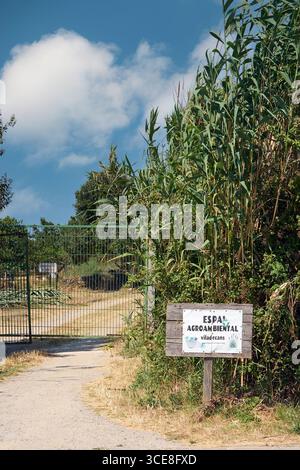 Viladecans. Barcelona - 16. August 2025: An einem sonnigen Tag steht am Eingang eines umzäunten Gartenbereichs ein Wegweiser für Espai Agroambiental. Stockfoto