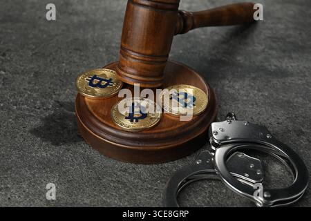 Kryptowährung. Bitcoins, Richtergabel und Handschellen auf grauem Tisch, Nahaufnahme Stockfoto