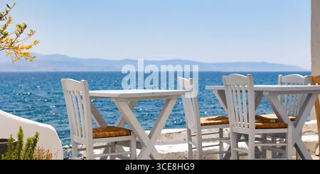 Esstisch und Stühle aus weißem Holz auf der Terrasse am Meer mit Blick auf das azurblaue Mittelmeer und Berge im Hintergrund Stockfoto