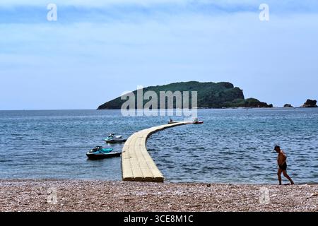 Mann in Badehosen, der an einem temporären Plastikdock am Budva Beach, Montenegro an der budva riviera vorbeiläuft Stockfoto
