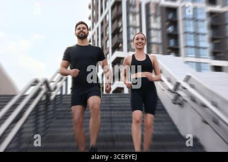 Frau und Mann in Sportbekleidung laufen draußen auf Treppen, Motion Blue-Effekt. Flachwinkelansicht Stockfoto