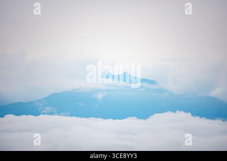 Ein atemberaubender Blick auf einen Berggipfel in Popayán, Cauca, Kolumbien, der aus einem Wolkenmeer unter einem weichen, bewölkten Himmel auftaucht. Stockfoto