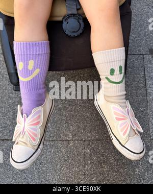 Kind mit nicht passenden bunten Socken und cremefarbenen Schuhen, die mit großen Schmetterlingsflügeln an den Zehen verziert sind und auf einem Kinderwagen sitzt Stockfoto