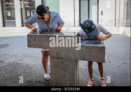 Madrid, Spanien. August 2025. Eine Frau und ein Junge trinken Wasser aus einem Brunnen an einem heißen Sommertag. Spanien steht in vielen Teilen der spanischen Halbinsel vor einer Hitzewelle mit extrem hohen Temperaturen von mehr als 40 Grad Celsius. Quelle: Marcos del Mazo/Alamy Live News Stockfoto