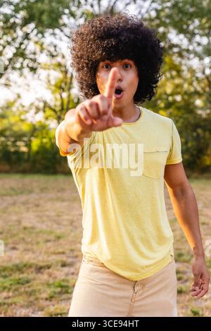 Junger Mann, der mit dem Finger im Park mit staunendem Ausdruck zeigt Stockfoto