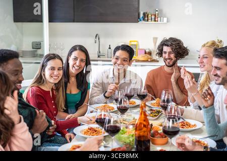 Eine Gruppe multikultureller Freunde genießt Spaghetti und Rotwein zu Hause. Freundschaft, italienische Küche, Zweisamkeit und fröhliches Essen in einer Bar Stockfoto