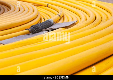 Neues leistungsstarkes Hochspannungskabel in gelbem Geflecht, verdrillt auf dem Boden. Stockfoto