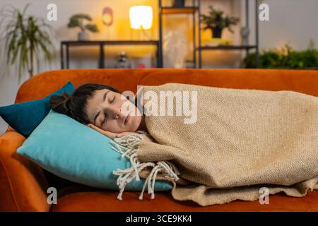 Müde kaukasische Frau, die ruhig mit Decke auf der Couch schläft. Glückliches Mädchen lächelnd auf der Couch schlafend bequem auf Kissen ruhig im Wohnzimmer. Gesundes Schlafkonzept. Stockfoto