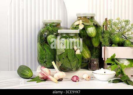 Eingelegte Gurken in Gläsern mit Knoblauch und Dill auf hölzernem Küchentisch, rustikaler Stil, hausgemachtes Beizrezept, Gurken und Zutaten zum Beizen, Stockfoto