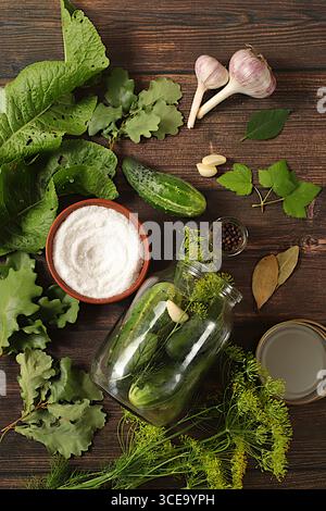 Hausgemachtes Beizrezept, Gurken und Beizzutaten, Hauskonservierungskonzept. Frisch eingelegte Gurken in einer Schüssel mit Knoblauch und Dill auf einem Beton Stockfoto