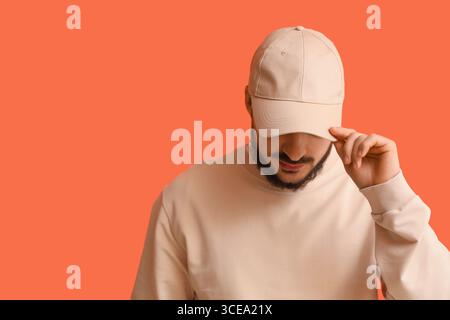 Schöner junger Mann in stilvoller Mütze auf orangefarbenem Hintergrund Stockfoto