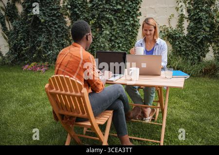Zwei junge Profis, die im Garten an Laptops arbeiten Stockfoto