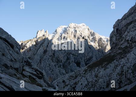Schneebedeckter Berggipfel unter einem klaren blauen Himmel, umgeben von rauem felsigem Gelände. Stockfoto