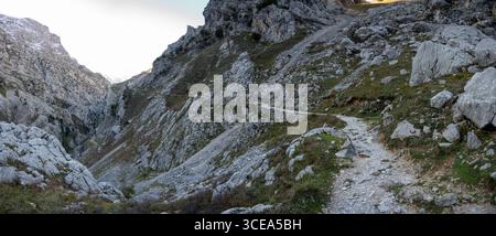 Bergpfad von Ruta del Cares im Nationalpark Picos de Europa in Spanien, der sich durch felsiges Gelände mit karger Vegetation schlängelt. Stockfoto