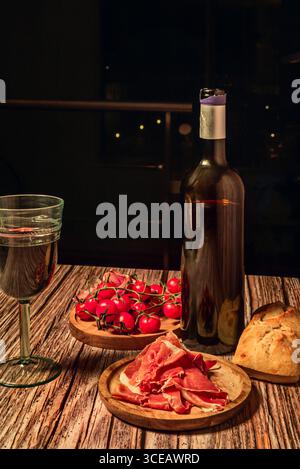 Farbharmonie: Ein Glas Roséwein neben Scheiben Jabugo-Schinken auf einer weißen Keramikplatte Stockfoto