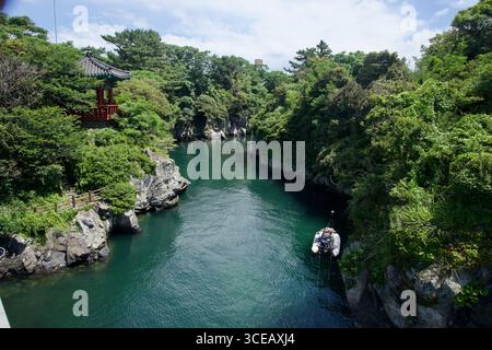 Grünes Wasser fließt zwischen Basaltklippen im Yongyeon Valley in Jeju City, mit einem traditionellen Pavillon am linken Ufer über dem schattigen Pfad. Stockfoto