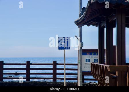 Entlang des Küstenweges neben einem hölzernen Pavillon und Geländern über dem Meer zeigt ein Schild für die Inselrundfahrt. Stockfoto