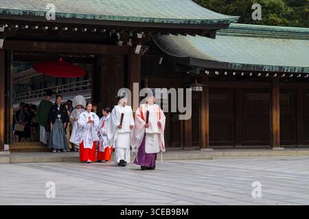 Shinto Hochzeit Prozession mit Braut trägt die traditionelle Watabōshi weiße Haube zu Fuß mit Bräutigam unter einem roten Regenschirm in der Meiji-Jingu-Shinto Stockfoto